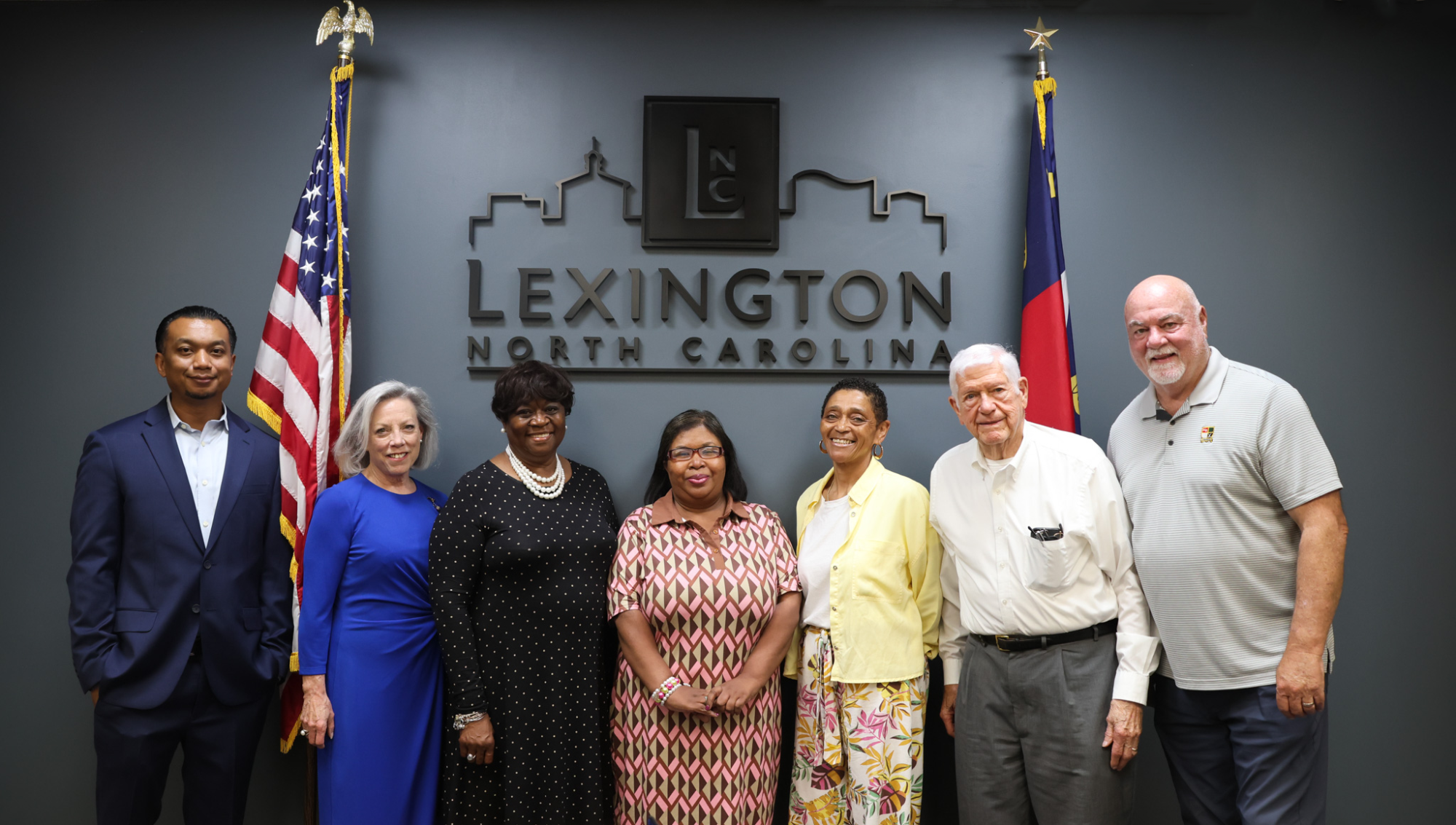 Photo of members of the Human Relations Commission standing in front of a City of Lexington Logo with the American & North Carolina flags next to them